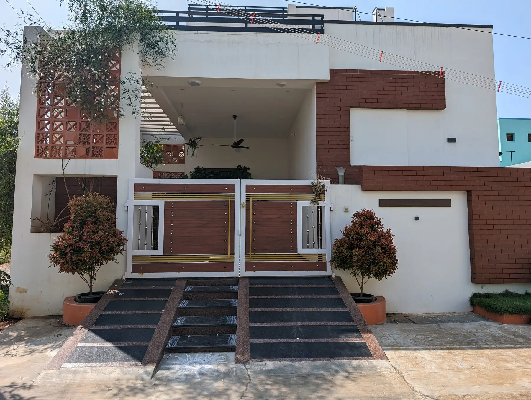 A finished single-storey modern home built by Poriyaalan — white render with red-brick cladding, a decorative jali screen and a wood-and-steel entrance gate